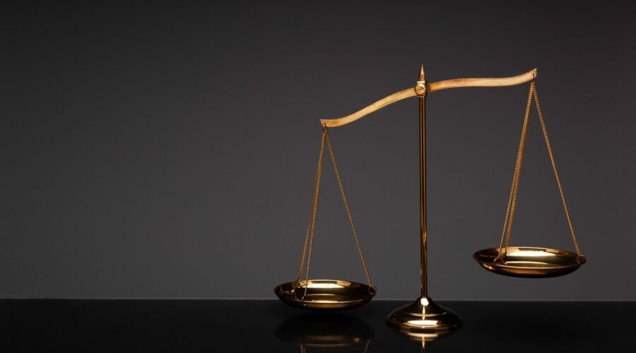 Gold brass balance scale, weight balance, imbalance scale with reflection on glass desktop with black background.